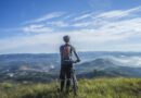 biker holding mountain bike on top of mountain with green grass